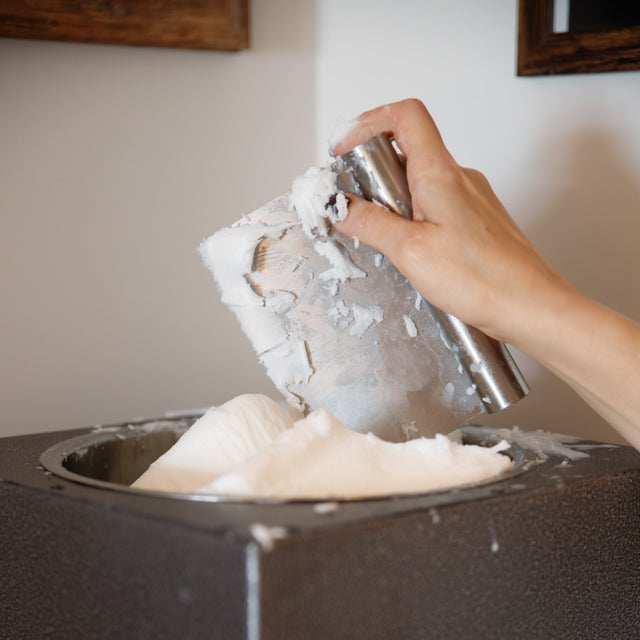 person putting wax in a melting pot to make candles