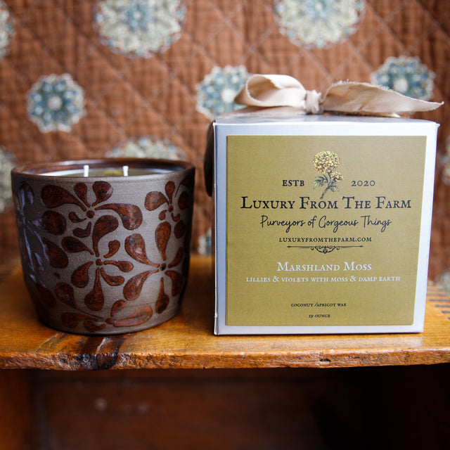 Ceramic candle with decorative pattern and 'Luxury From The Farm' packaging on a wooden surface.