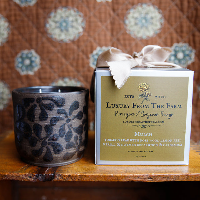 Ceramic candle and branded box on a wooden surface with a patterned fabric background luxury form the farm candle sent mulch