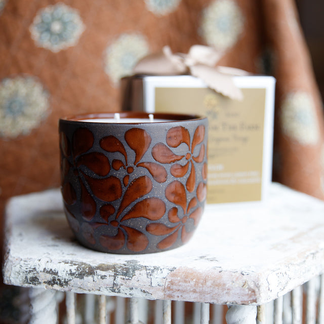 Decorative ceramic pot with floral patterns on a white surface with a patterned fabric background.